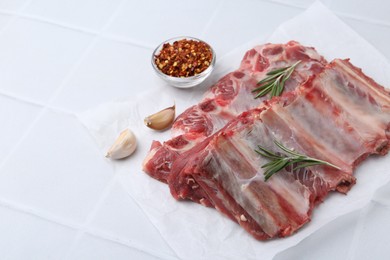 Photo of Fresh raw beef ribs and spices on white tiled table, closeup. Space for text