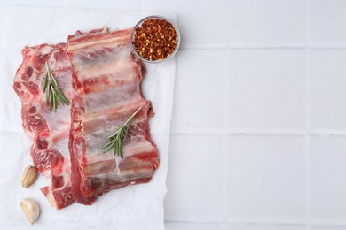 Photo of Fresh raw beef ribs and spices on white tiled table, flat lay. Space for text