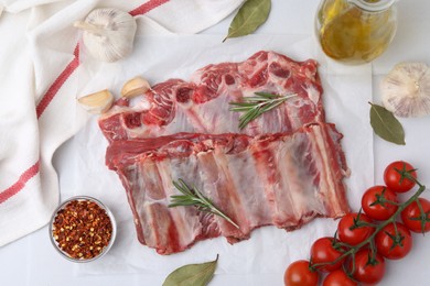Photo of Fresh raw beef ribs, tomatoes and spices on white table, flat lay