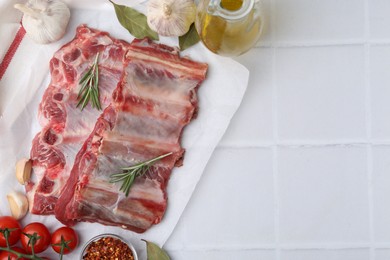 Photo of Fresh raw beef ribs, tomatoes and spices on white tiled table, flat lay. Space for text