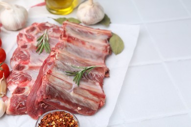 Photo of Fresh raw beef ribs and spices on white tiled table, closeup. Space for text