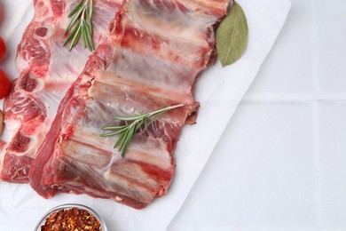 Photo of Fresh raw beef ribs and spices on white tiled table, top view. Space for text