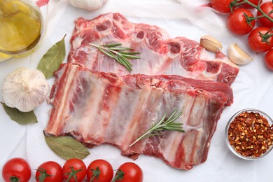 Photo of Fresh raw beef ribs, tomatoes and spices on white table, flat lay