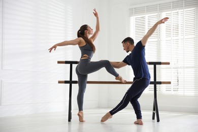 Photo of Couple of professional dancers stretching at barre in studio