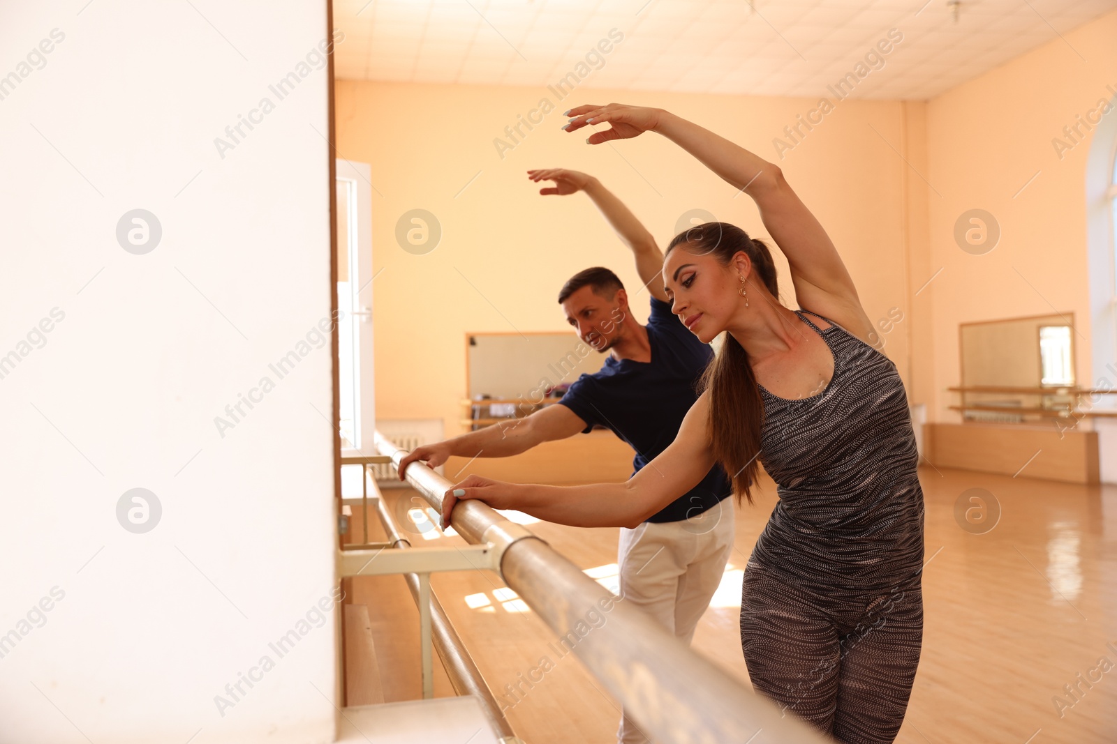 Couple of professional dancers stretching at barre in studio, selective focus Photo of Couple of professional dancers stretching at barre in studio, selective focus