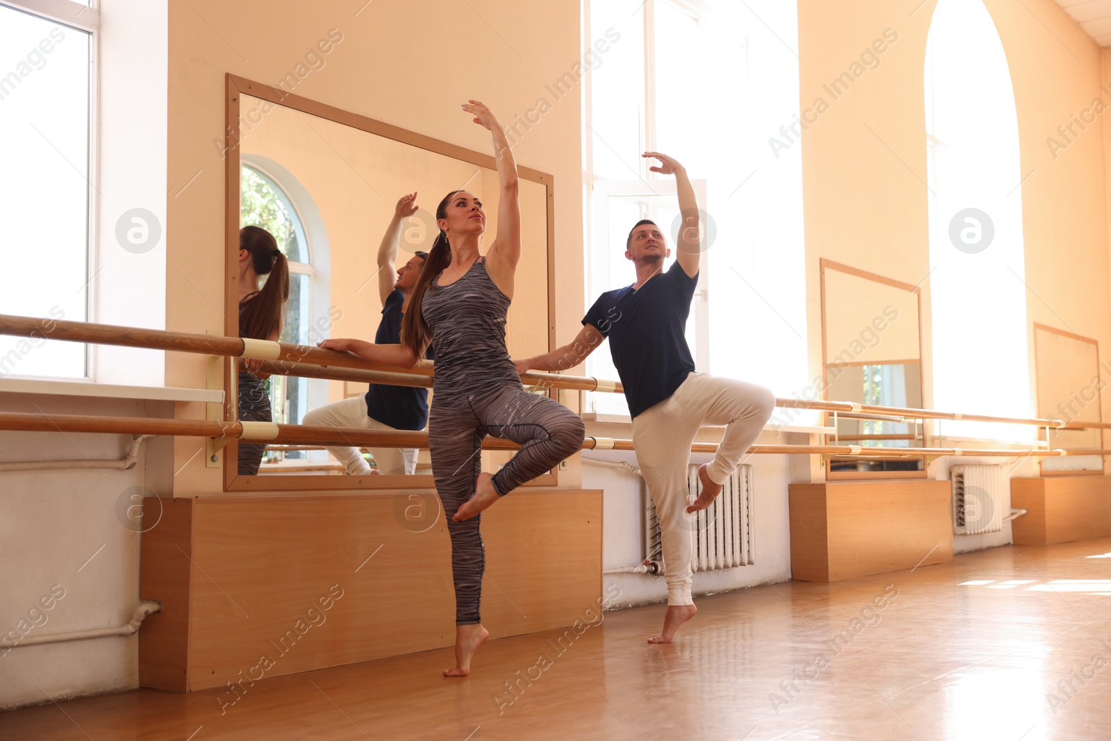 Couple of professional dancers stretching at barre in studio Photo of Couple of professional dancers stretching at barre in studio