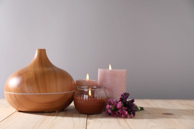 Photo of Spa composition with flowers and burning candles on wooden table against grey background, closeup