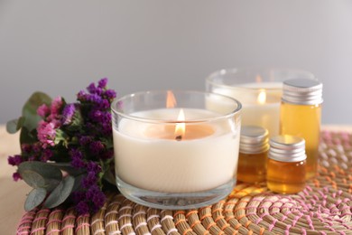 Photo of Burning candles, flowers and bottles of cosmetic products on table against grey background, closeup