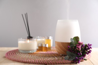 Photo of Spa composition with burning candles and aroma oil diffuser on wooden table against light grey background, closeup