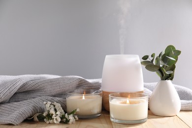 Photo of Spa composition with burning candles and aroma oil diffuser on wooden table against light grey background, closeup