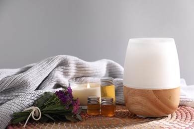 Photo of Spa composition with burning candle and aroma oil diffuser on table against light grey background, closeup