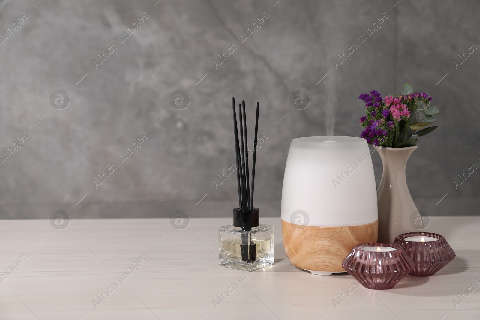 Spa composition with burning candles and aroma oil diffuser on white wooden table near grey wall, space for text Photo of Spa composition with burning candles and aroma oil diffuser on white wooden table near grey wall, space for text