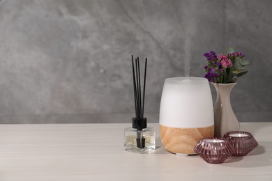 Photo of Spa composition with burning candles and aroma oil diffuser on white wooden table near grey wall, space for text
