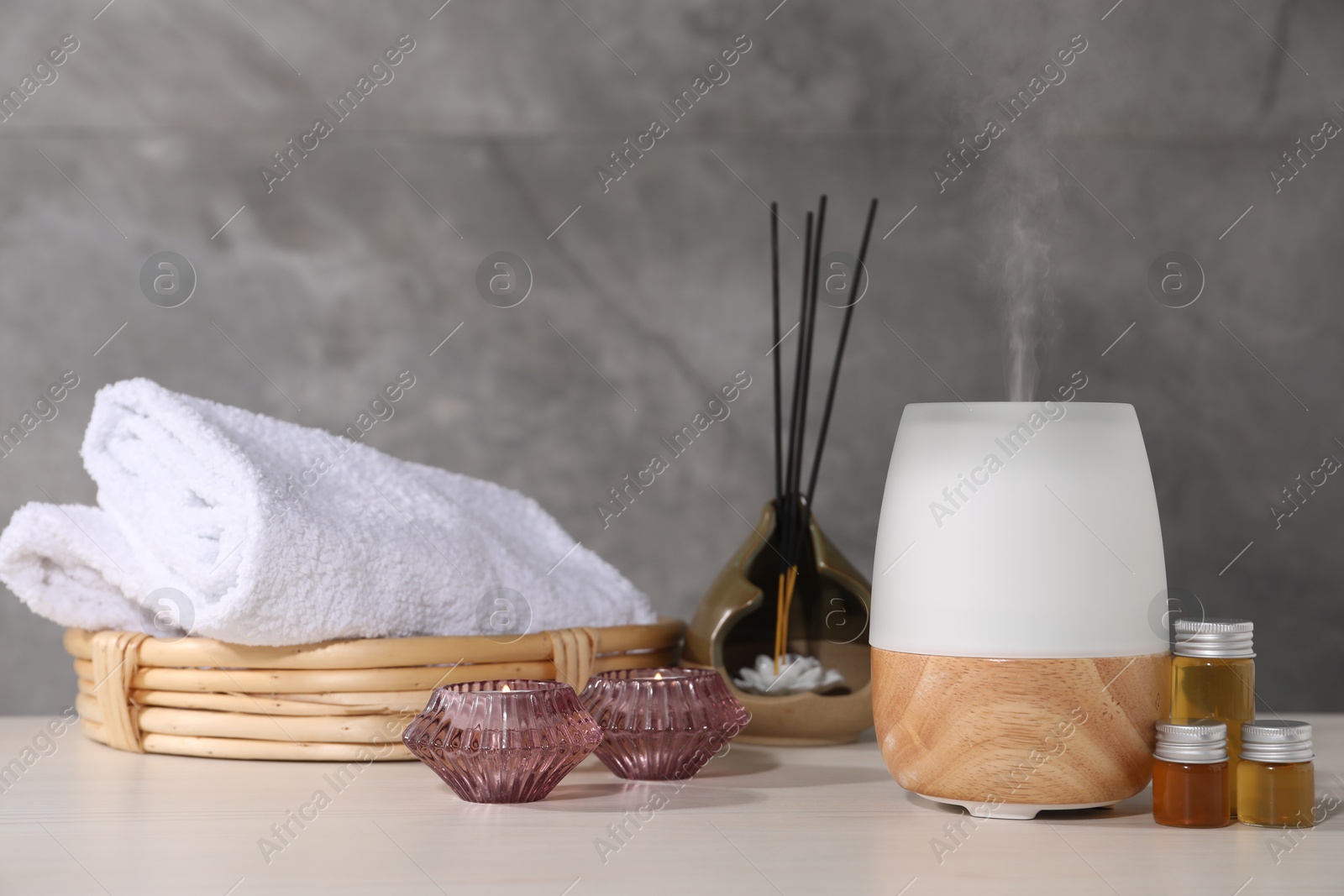 Spa composition with burning candles and aroma oil diffuser on white wooden table near grey wall, closeup Photo of Spa composition with burning candles and aroma oil diffuser on white wooden table near grey wall, closeup
