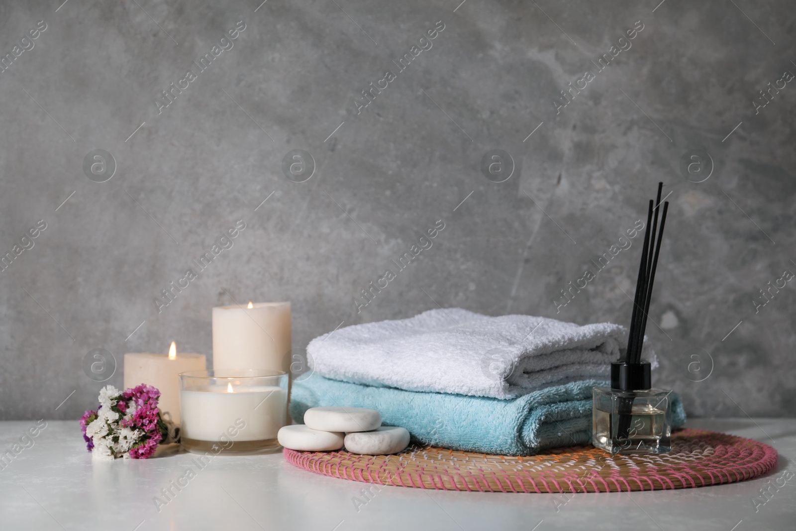 Spa composition with burning candles on white wooden table near grey wall Photo of Spa composition with burning candles on white wooden table near grey wall