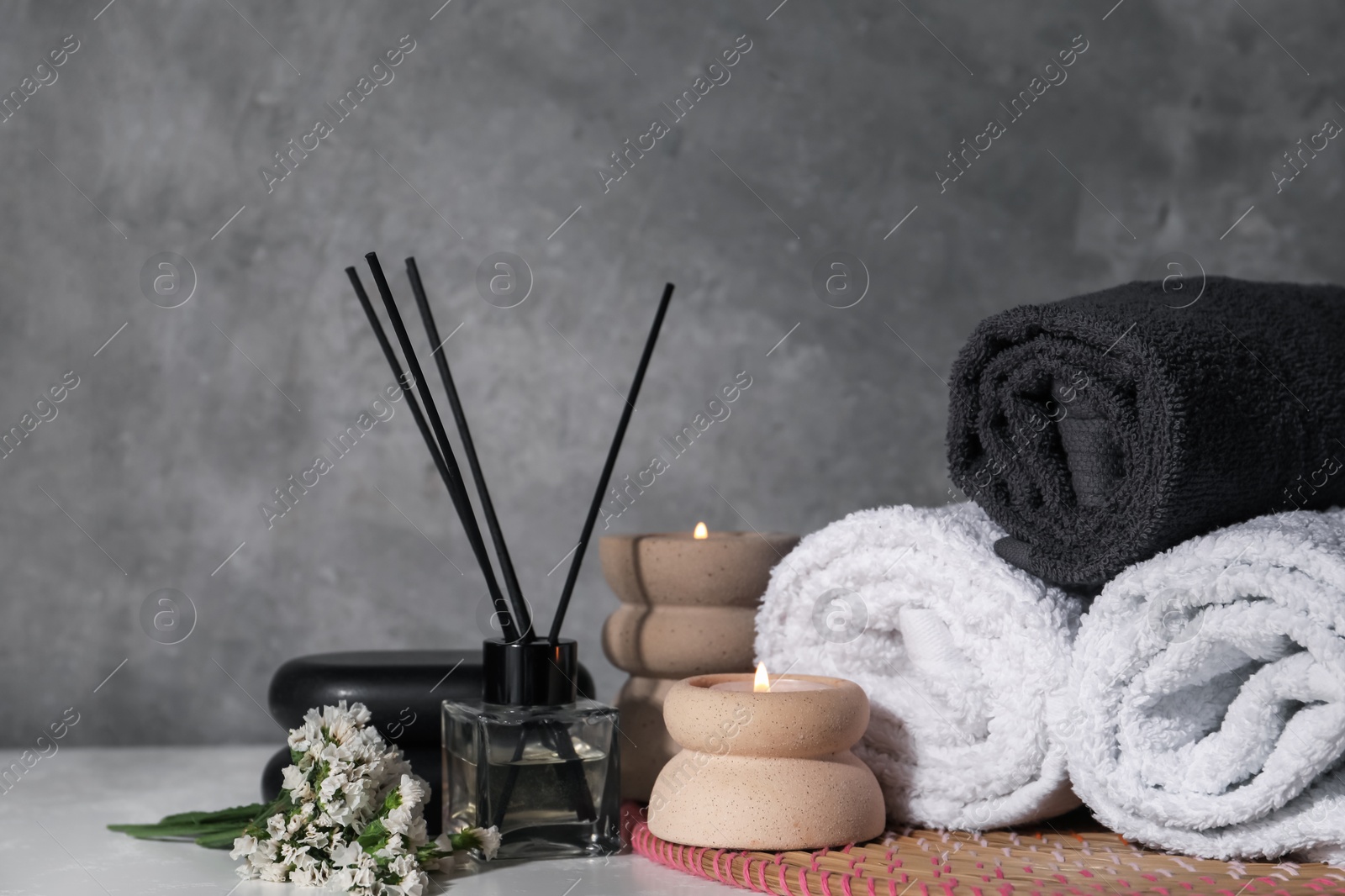 Spa composition with burning candles on white wooden table near grey wall Photo of Spa composition with burning candles on white wooden table near grey wall