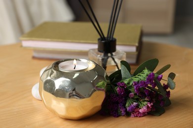 Photo of Spa composition with burning candle and reed diffuser on wooden table indoors, closeup