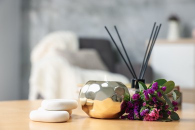 Photo of Spa composition with burning candle and reed diffuser on wooden table indoors, closeup