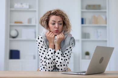 Photo of Air conditioning. Woman with scarf suffering from cold temperature at workplace in office