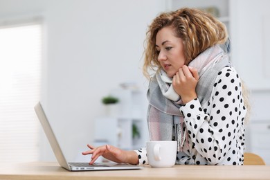 Photo of Air conditioning. Woman with scarf suffering from cold temperature at workplace in office