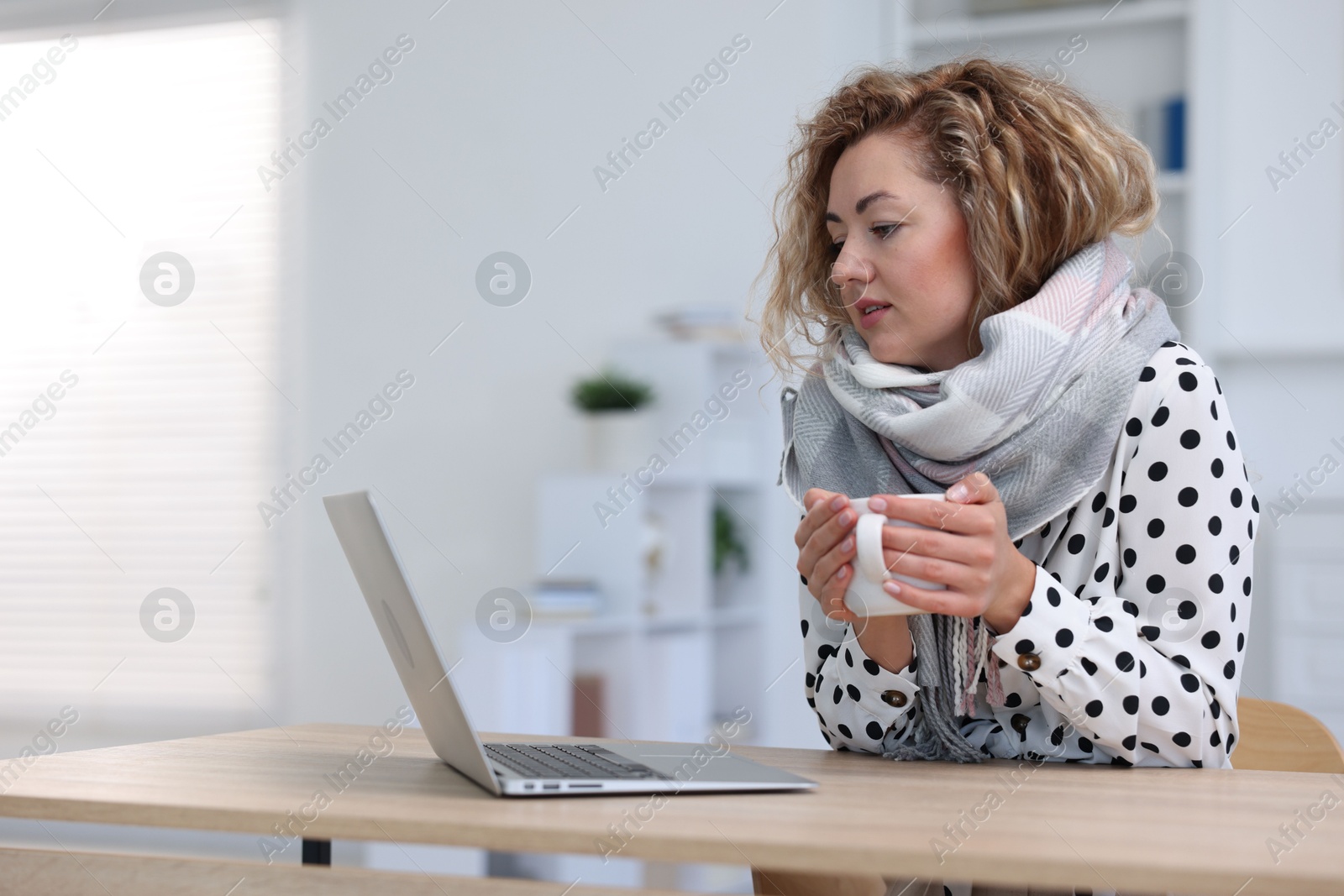 Air conditioning. Woman with scarf and cup of hot drink suffering from cold temperature at workplace in office Photo of Air conditioning. Woman with scarf and cup of hot drink suffering from cold temperature at workplace in office