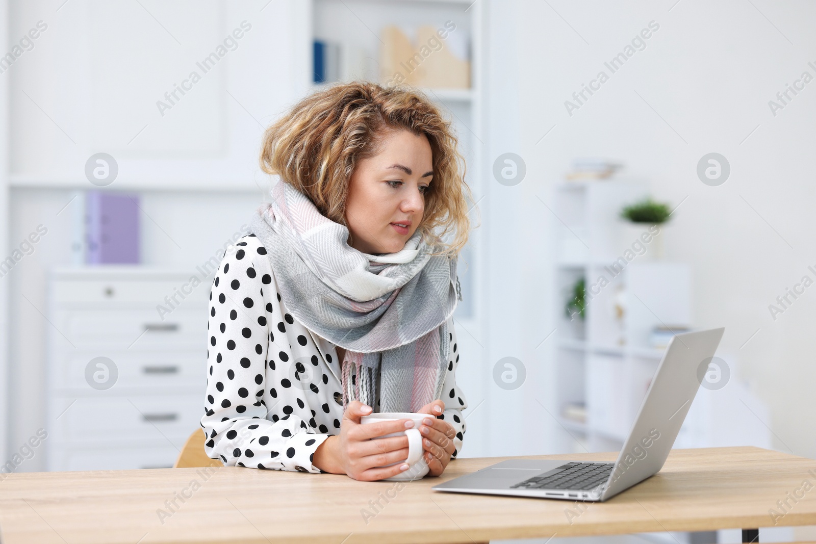 Air conditioning. Woman with scarf and cup of hot drink suffering from cold temperature at workplace in office Photo of Air conditioning. Woman with scarf and cup of hot drink suffering from cold temperature at workplace in office