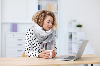 Photo of Air conditioning. Woman with scarf and cup of hot drink suffering from cold temperature at workplace in office