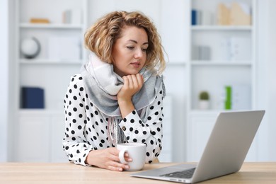 Photo of Air conditioning. Woman with scarf and cup of hot drink suffering from cold temperature at workplace in office