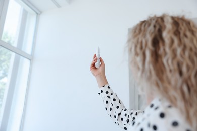 Photo of Woman using remote to control air conditioner in office, back view