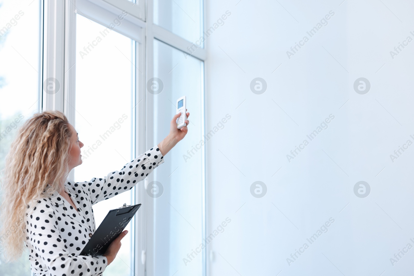 Woman using remote to control air conditioner in office, back view Photo of Woman using remote to control air conditioner in office, back view