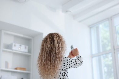 Photo of Woman using remote to control air conditioner in office, back view
