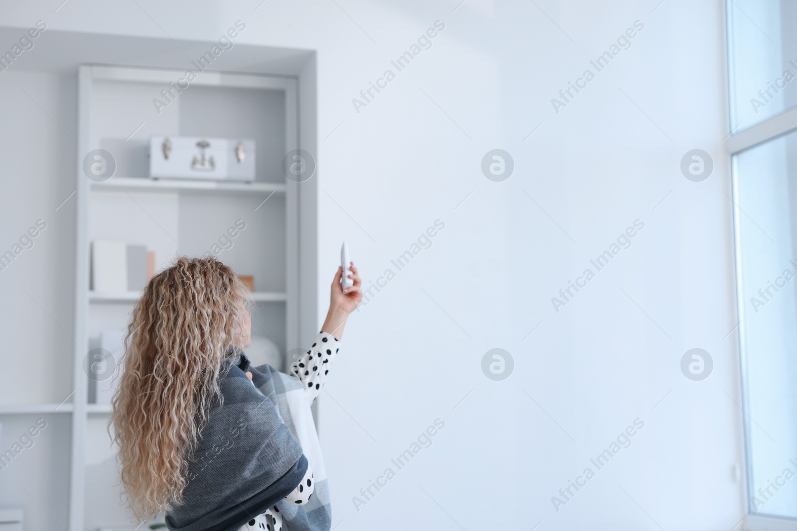 Woman using remote to control air conditioner in office, back view Photo of Woman using remote to control air conditioner in office, back view