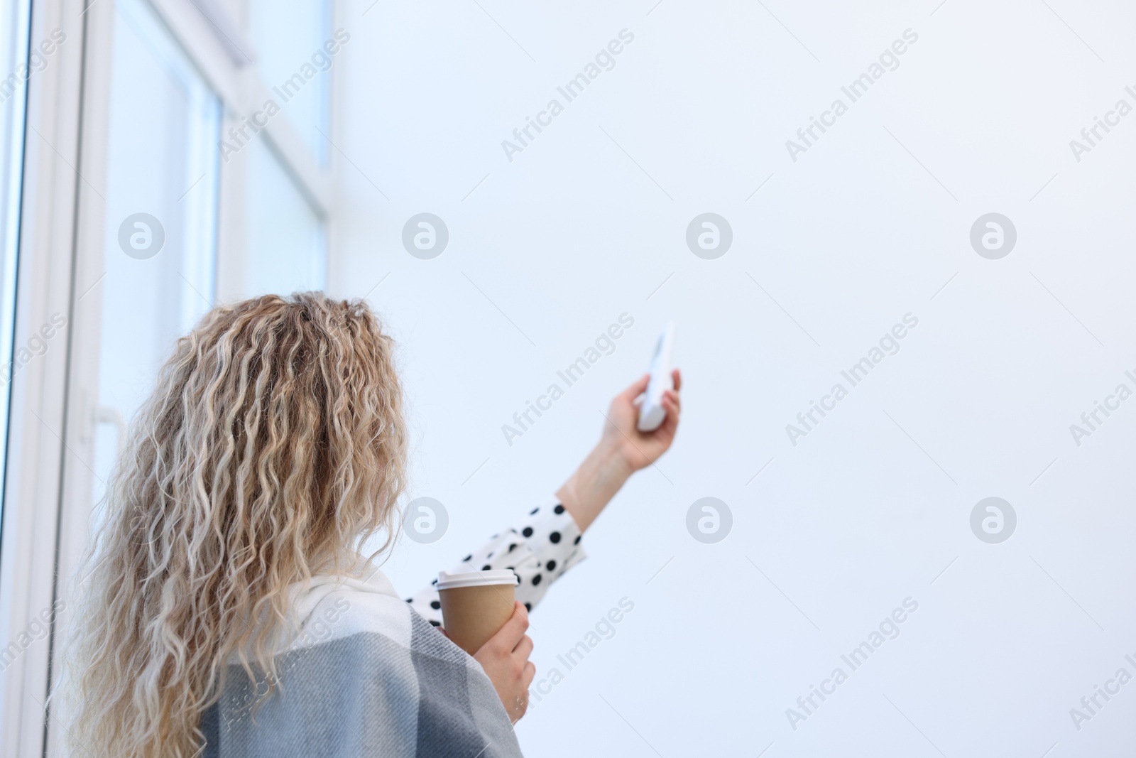 Woman using remote to control air conditioner in office, back view Photo of Woman using remote to control air conditioner in office, back view