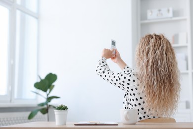 Photo of Woman using remote to control air conditioner in office, back view