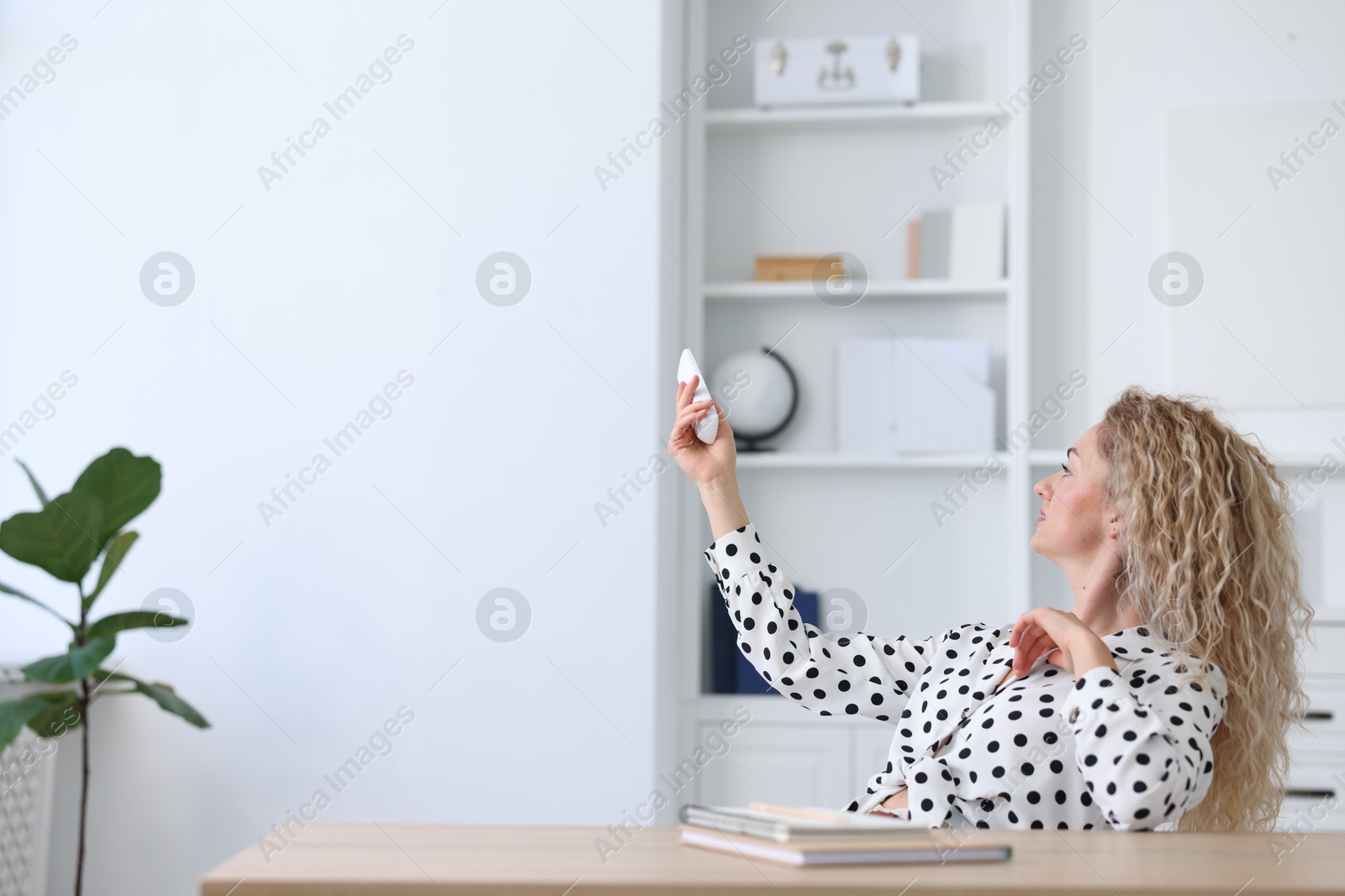 Woman using remote to control air conditioner in office Photo of Woman using remote to control air conditioner in office