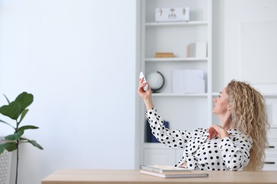 Photo of Woman using remote to control air conditioner in office