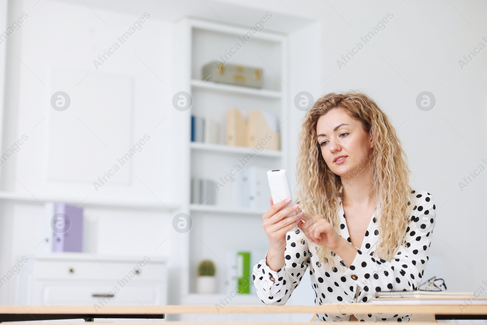 Woman using remote to control air conditioner in office Photo of Woman using remote to control air conditioner in office