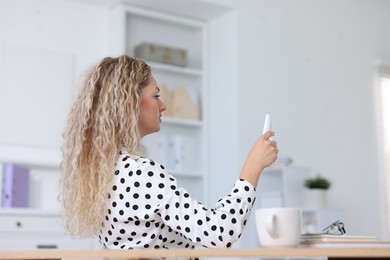 Photo of Woman using remote to control air conditioner in office
