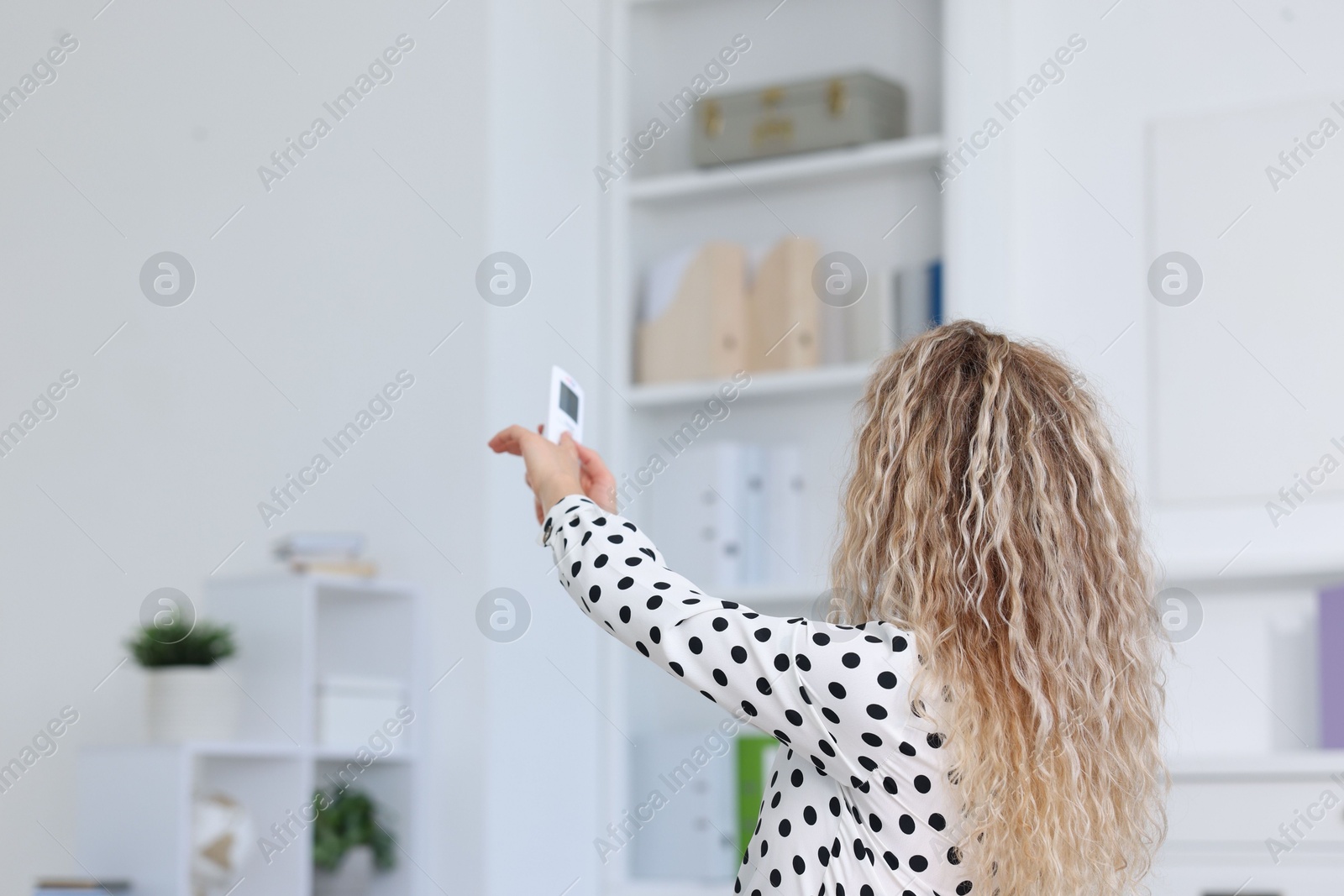Woman using remote to control air conditioner in office, back view Photo of Woman using remote to control air conditioner in office, back view