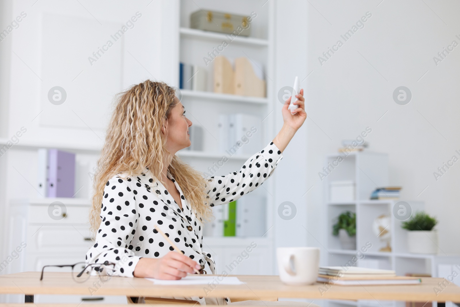 Woman using remote to control air conditioner in office Photo of Woman using remote to control air conditioner in office