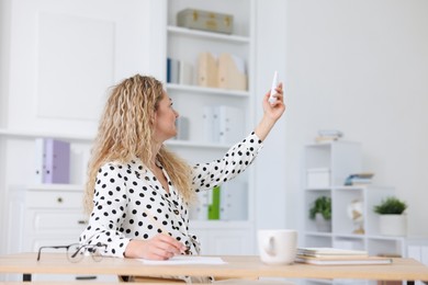 Photo of Woman using remote to control air conditioner in office
