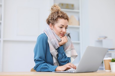 Photo of Air conditioning. Woman with scarf suffering from cold temperature at workplace in office