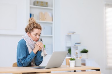 Photo of Air conditioning. Woman with scarf suffering from cold temperature at workplace in office