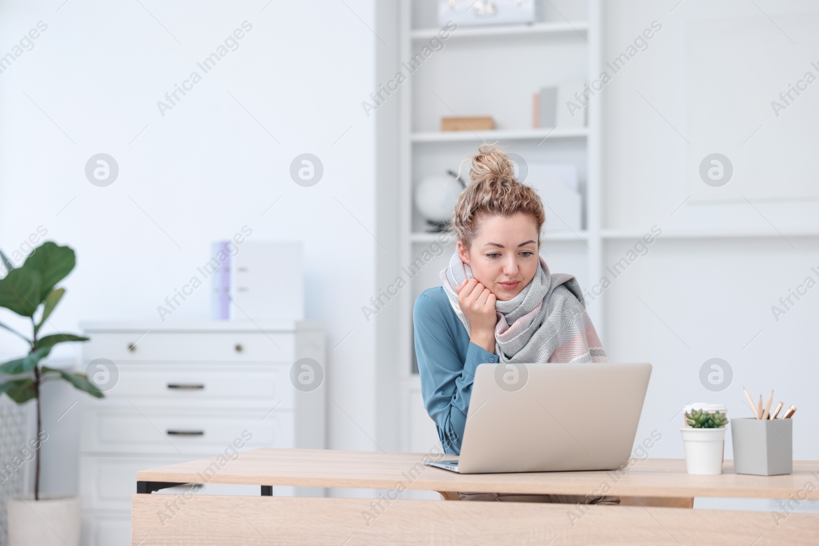 Photo of Air conditioning. Woman with scarf suffering from cold temperature at workplace in office