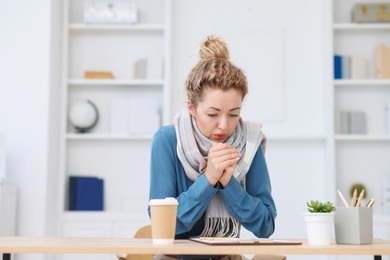 Photo of Air conditioning. Woman with scarf suffering from cold temperature at workplace in office