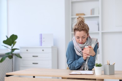 Photo of Air conditioning. Woman with scarf suffering from cold temperature at workplace in office