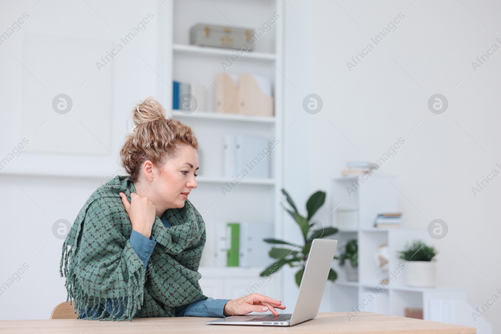 Photo of Air conditioning. Woman with scarf suffering from cold temperature at workplace in office