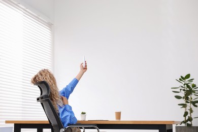 Photo of Woman using remote to control air conditioner in office, back view