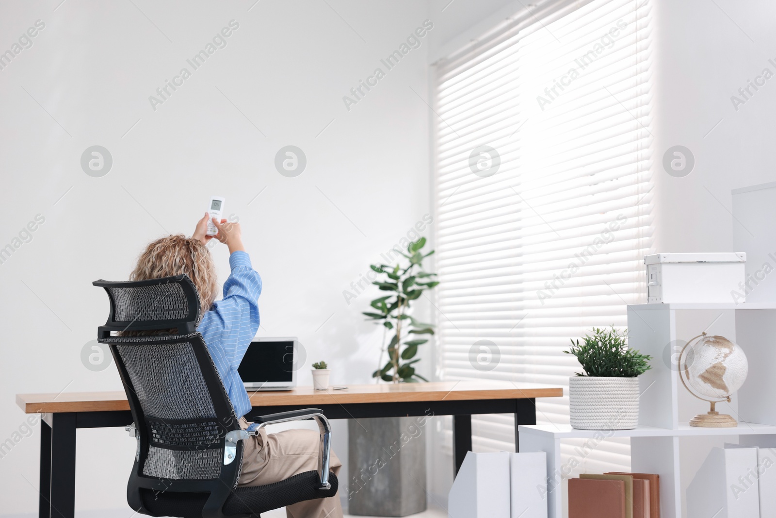 Woman using remote to control air conditioner in office, back view Photo of Woman using remote to control air conditioner in office, back view