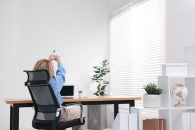 Photo of Woman using remote to control air conditioner in office, back view